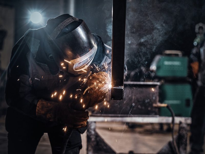 Man is working at metal factory, he is welding a piece of rail using special tools.