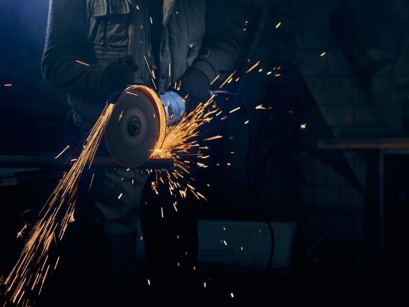 Close up of fitter in special suit cutting with rotating disc for metal with large sparks. Concept of process polishing or welding metal with flash sparks in factory.
